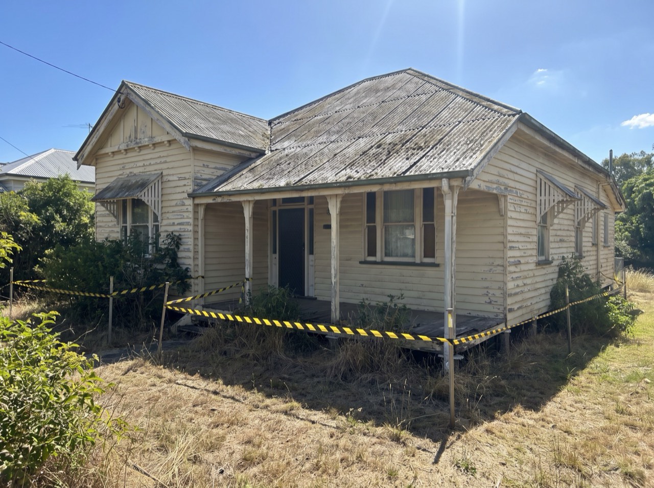 Before: a Queenslander home with an aged asbestos-look roof, hazard tape around the property