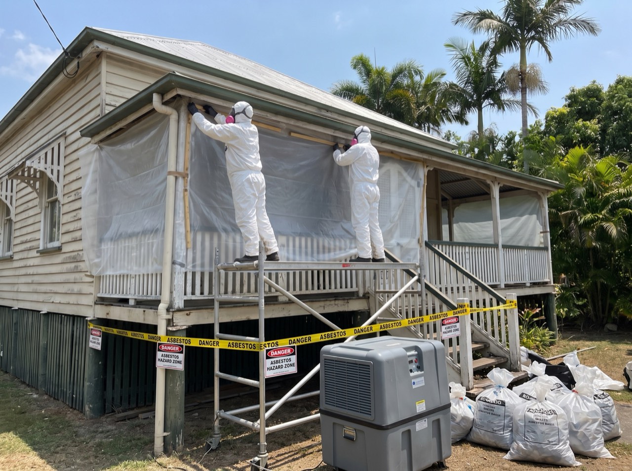 Crew setting up containment sheeting around a Queenslander roofline