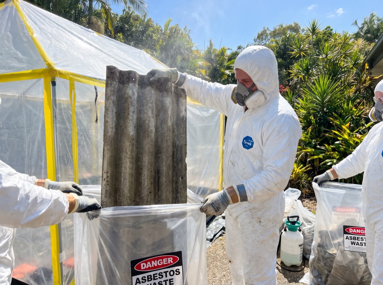 Removal in progress, roof sheeting handled by hand into a labelled waste bag