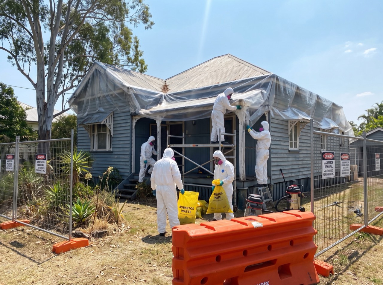 An older Ipswich-style timber cottage mid-removal, crew and containment at the roofline